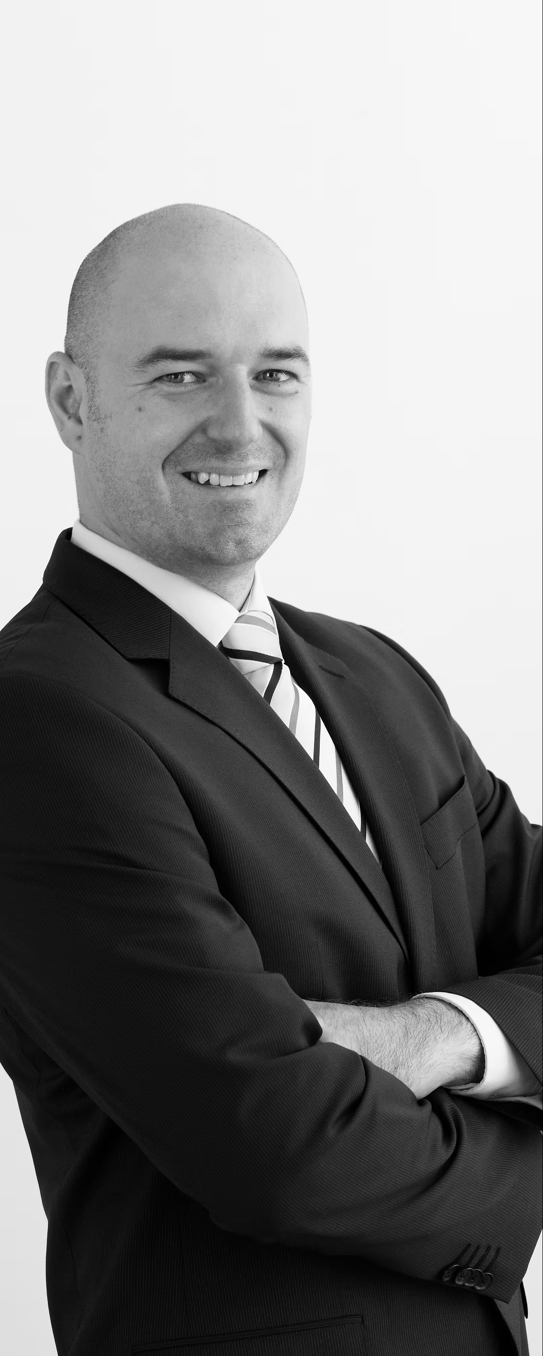 Photo of Michael Auinger, smiling, standing, hands crossed in front of body, wearing a dark suit